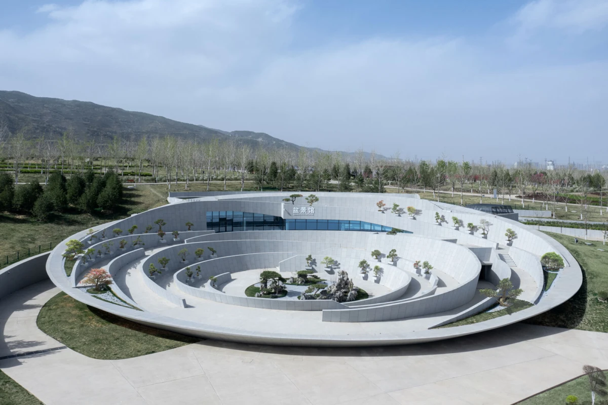 Spiral concrete amphitheater with terraced rings of trees, set in a park against distant hills under a blue sky.
