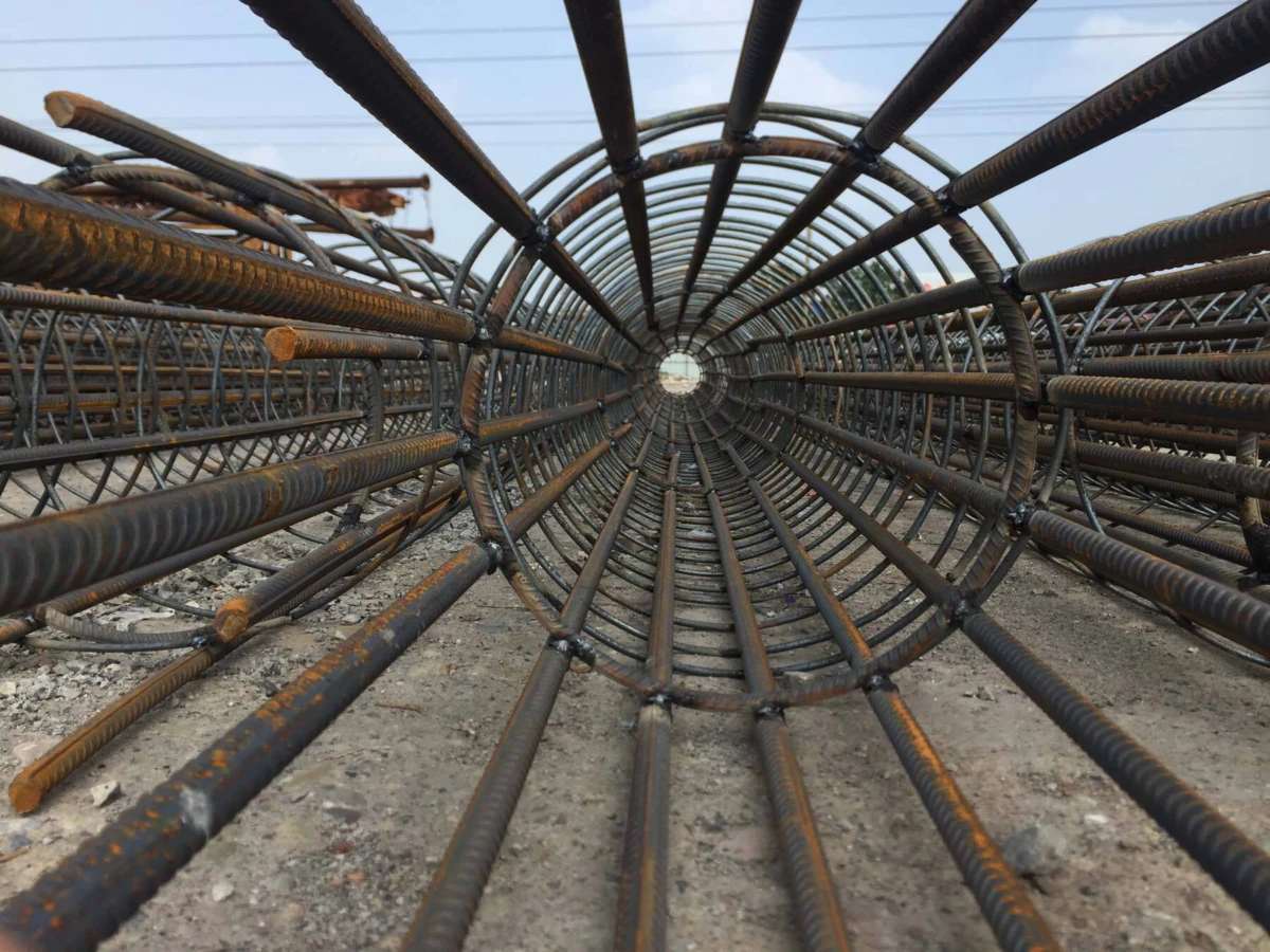 Circular tunnel of rusted steel rebar arranged in concentric rings at a construction site, viewed from inside.