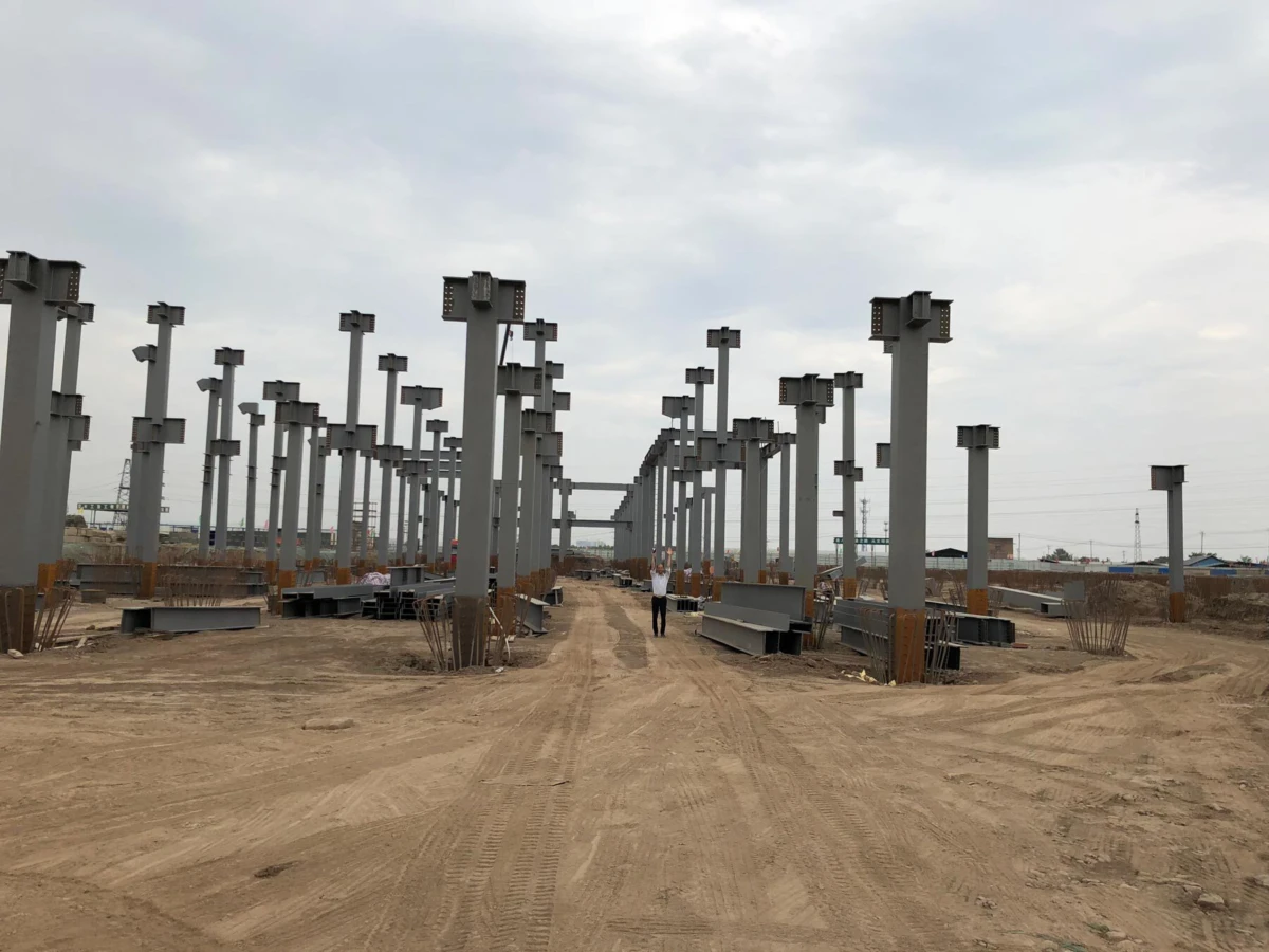 Person standing between rows of tall gray concrete columns at an outdoor construction site on dirt ground.
