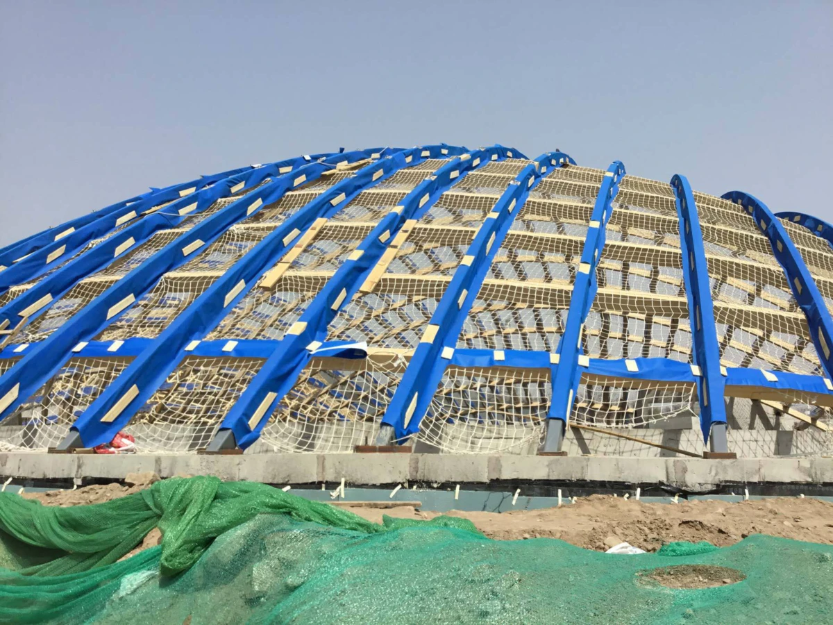 Blue arched framework forming a domed construction at an outdoor site, with green tarpaulin in the foreground.