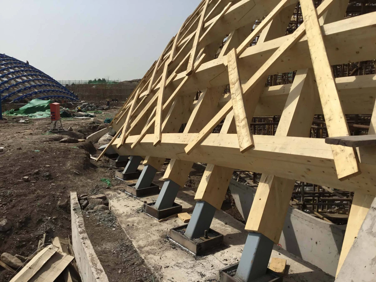 Timber formwork with diagonal bracing installed on steel bases at a dirt construction site.
