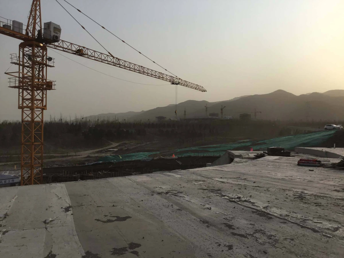 Yellow tower crane dominates a construction site at dusk, with concrete slab foreground and distant hills.