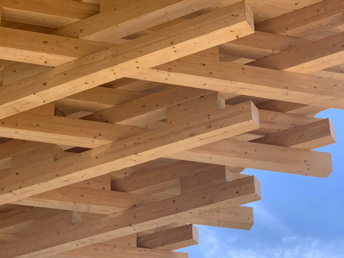 Overlapping pine beams arranged in a timber frame outdoors against a blue sky.