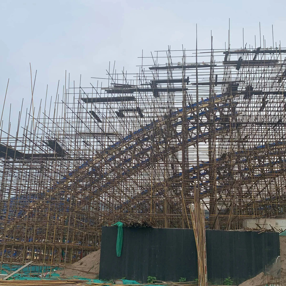 Dense bamboo scaffolding surrounding a partially built building at an outdoor construction site.