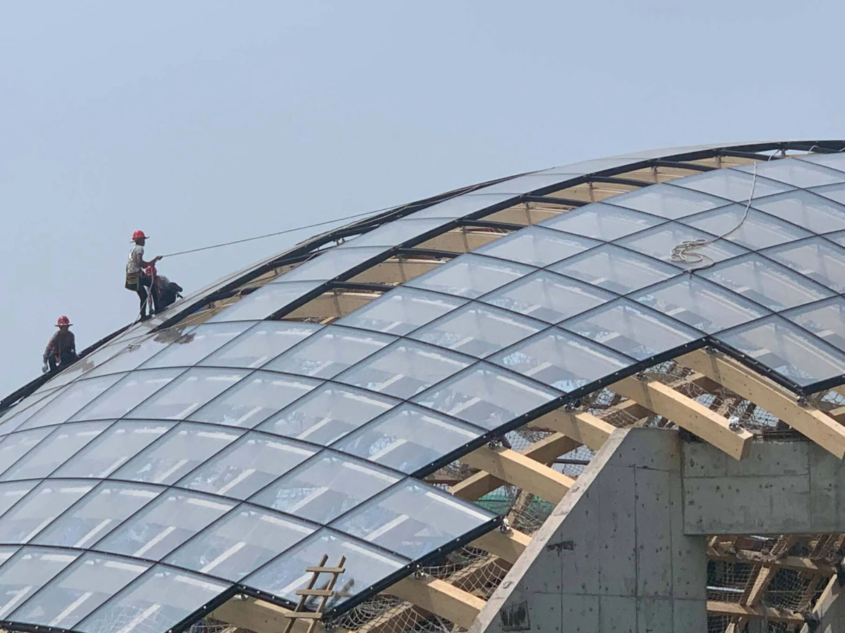 Construction workers wearing red helmets on a curved glass skylight during installation.