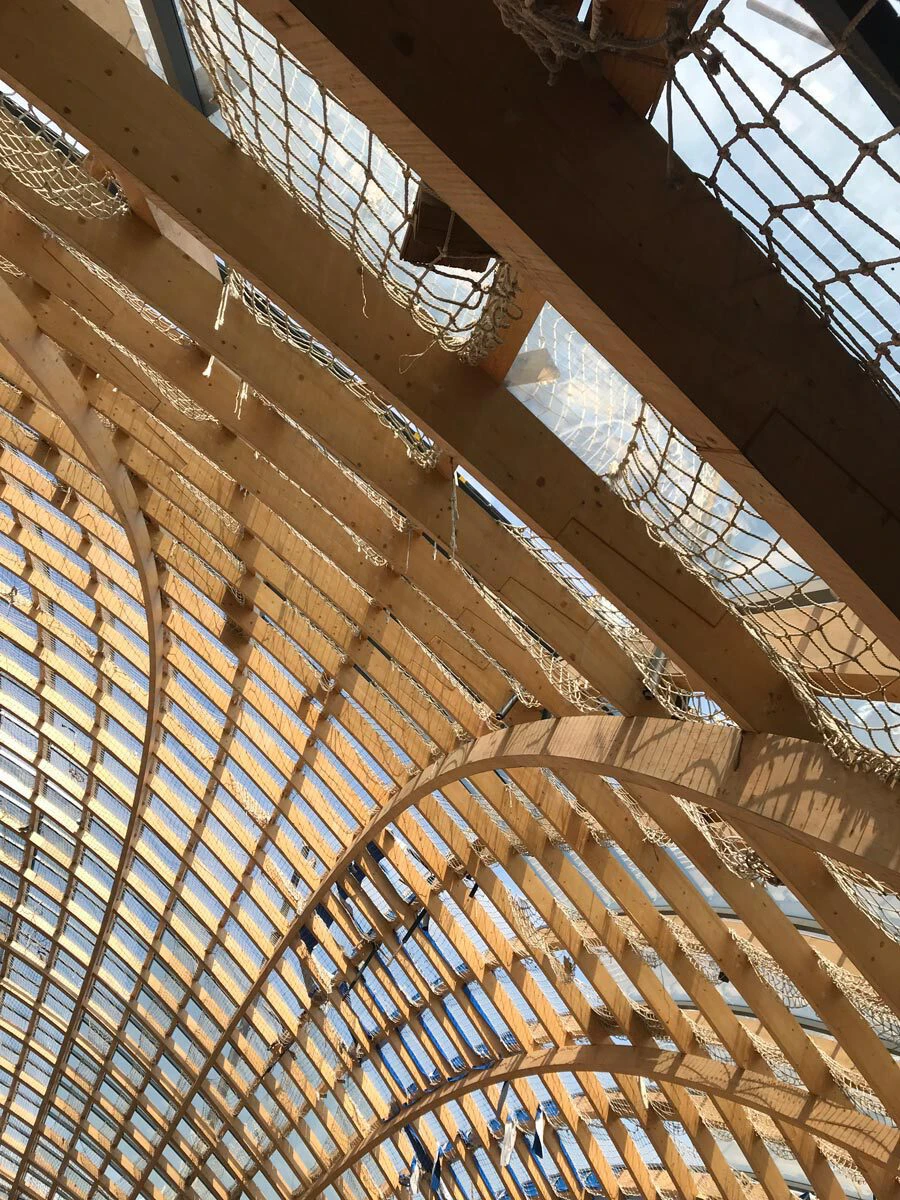 Timber arch roof under construction with curved wooden ribs and protective netting.