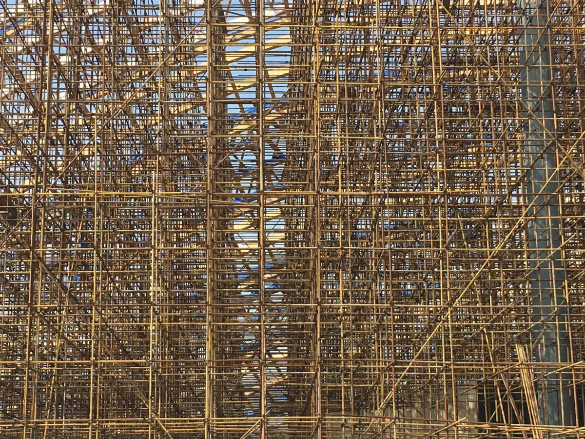 Dense steel scaffolding forms a lattice around a building under construction.