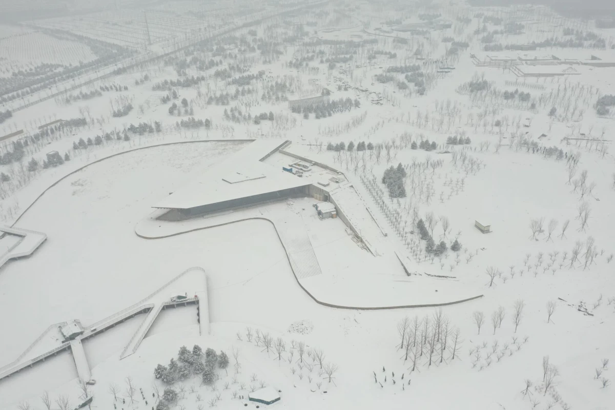 Aerial view of a snow-covered modern architectural complex with curved and angular roofs in a wintry landscape.