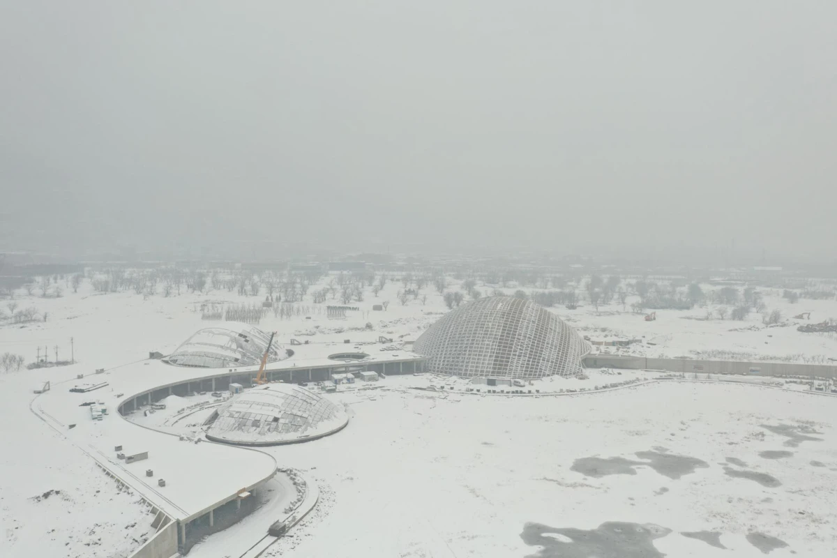 Aerial view of interconnected geodesic glass domes linked by curved walkway in a snow-covered landscape.