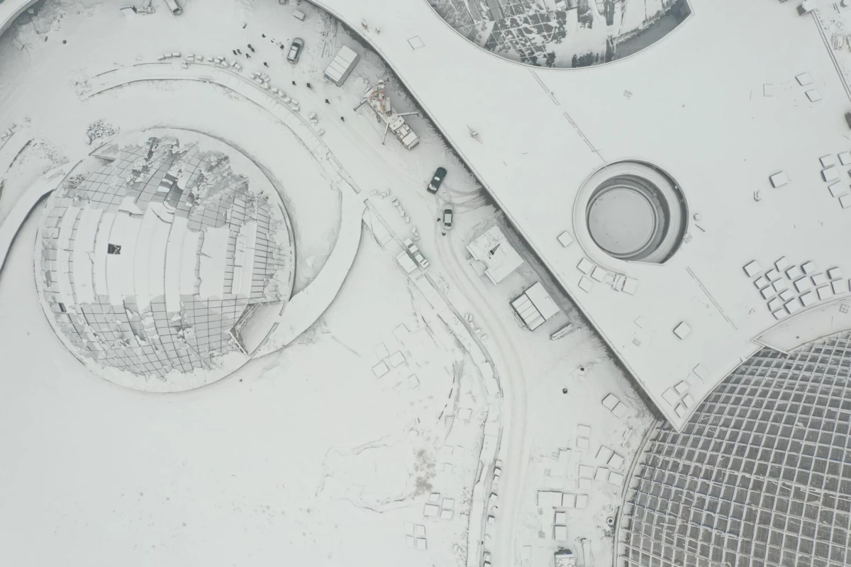 Snow-covered aerial view of a complex featuring a large glass-domed sphere and circular structures, with vehicles on surrounding roads.