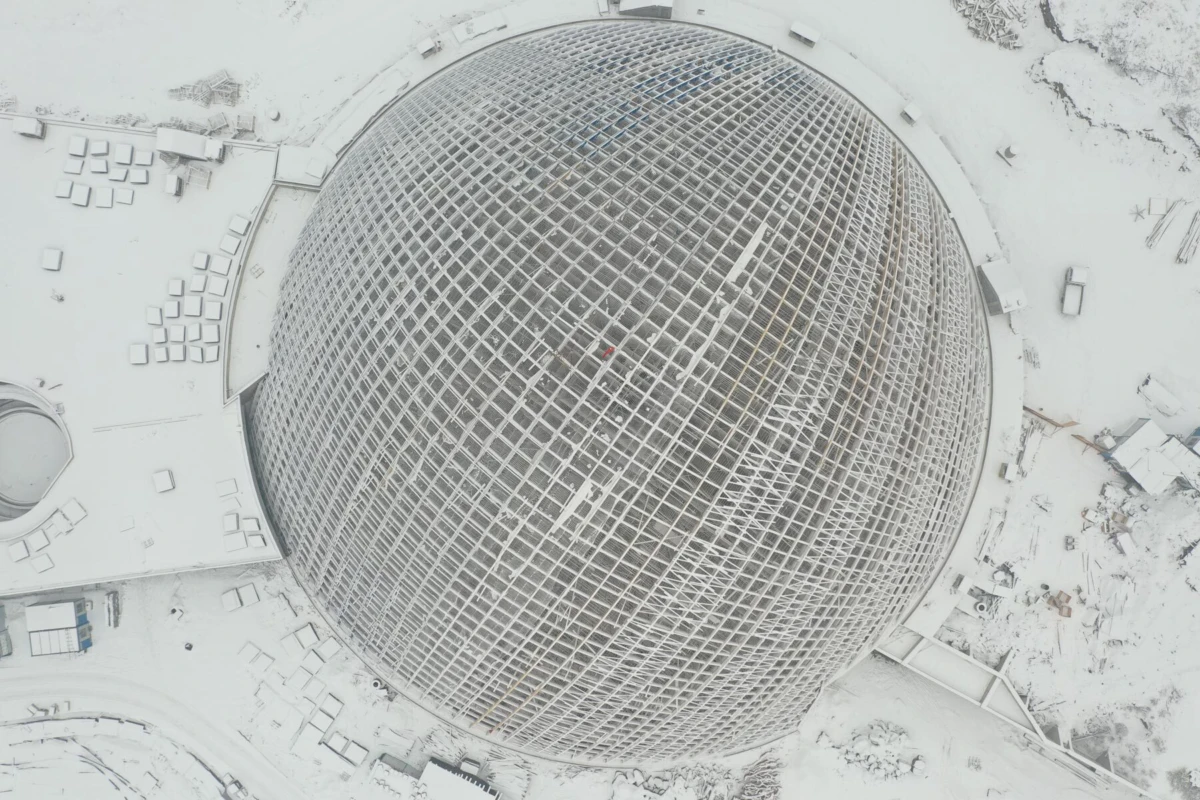 Aerial view of a large circular geodesic dome under construction in a snow-covered landscape.