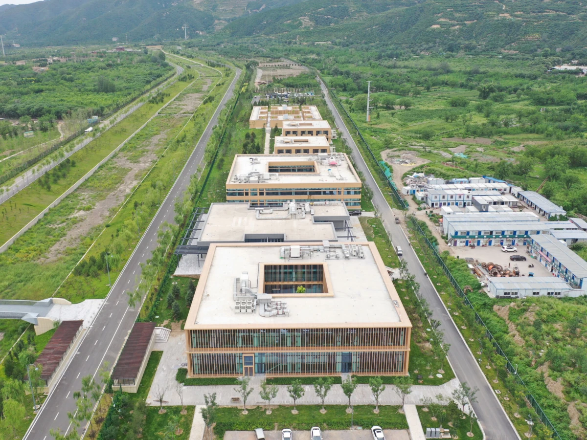 Aerial view of a modern office campus with beige rectangular buildings lined along a central road, amid green fields.