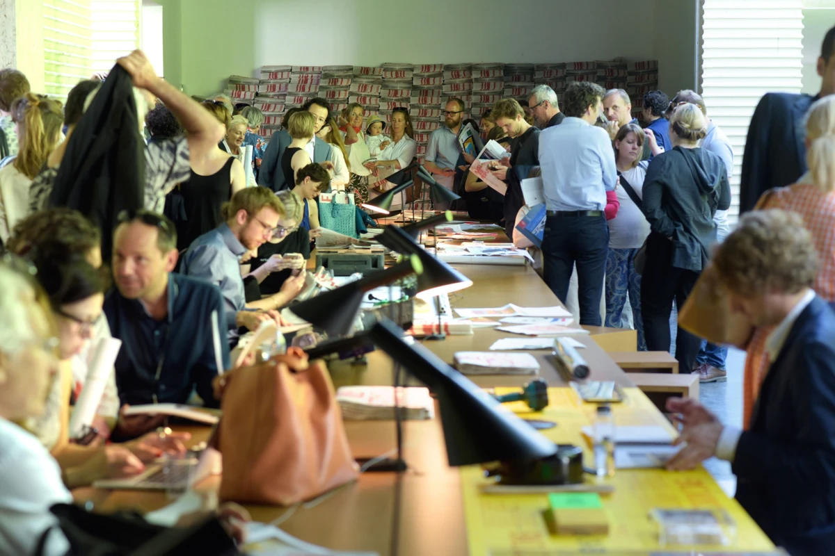Several authors sign books at long tables in a crowded bookstore during a book signing event.