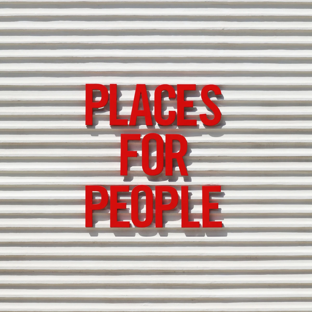 Red three-line sign reading "PLACES FOR PEOPLE" on a white corrugated wall.