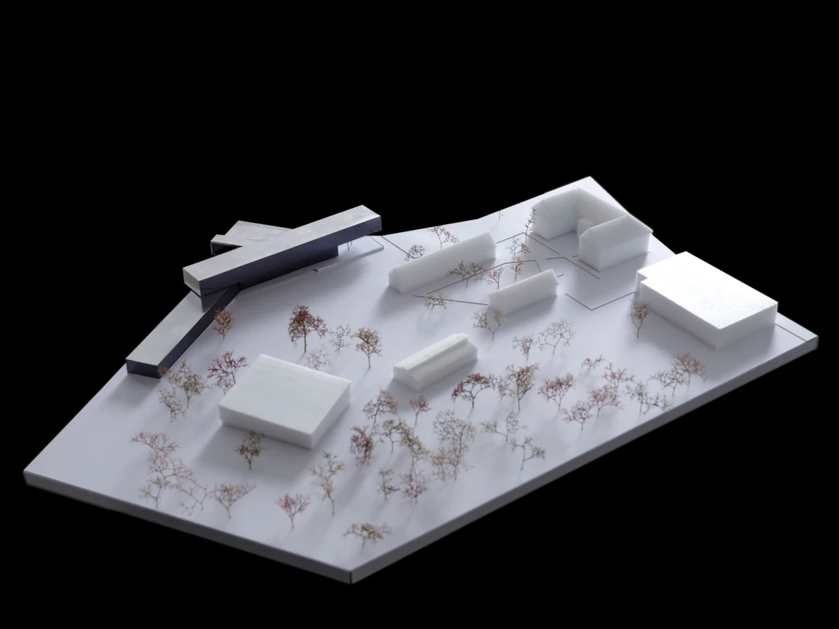 Scale architectural model of an urban site with white foam buildings, a dark linear feature, and sparse trees on a white base.