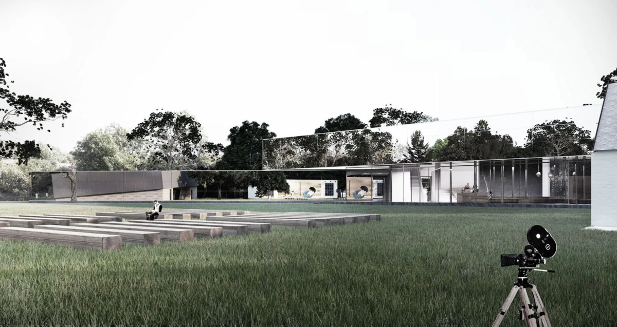 Camera on a tripod in the foreground; modern glass-walled building across a grassy lawn; a person sits on stone steps in the distance.