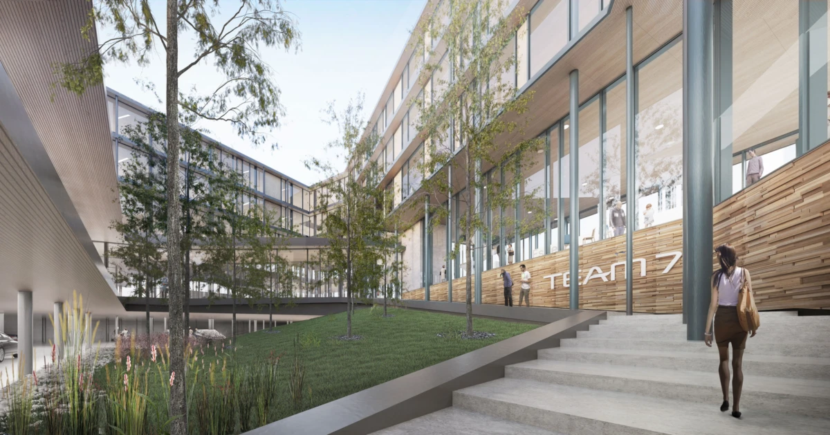 Person ascending concrete stairs beside a glass-walled modern campus building with trees and greenery.