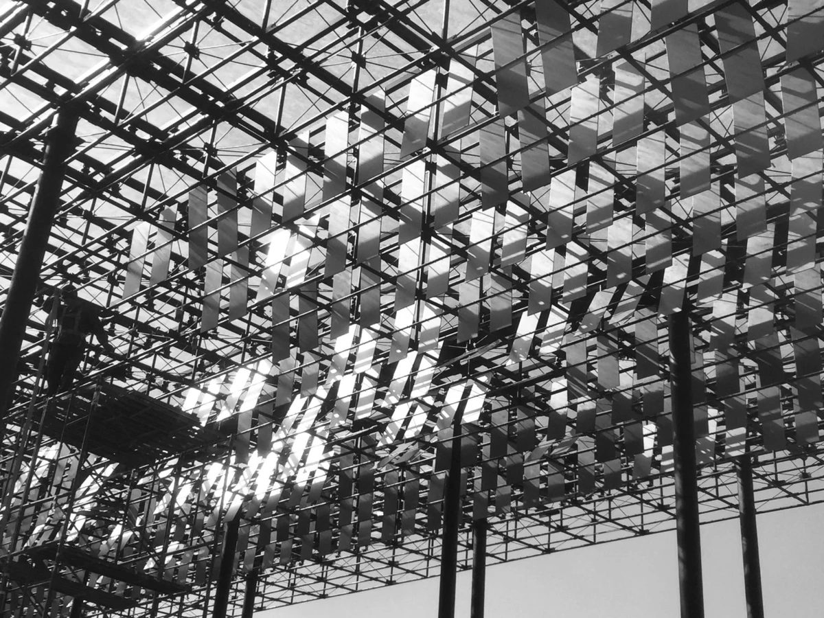 Intricate steel framework with rows of rectangular banners hanging overhead under a glass canopy.