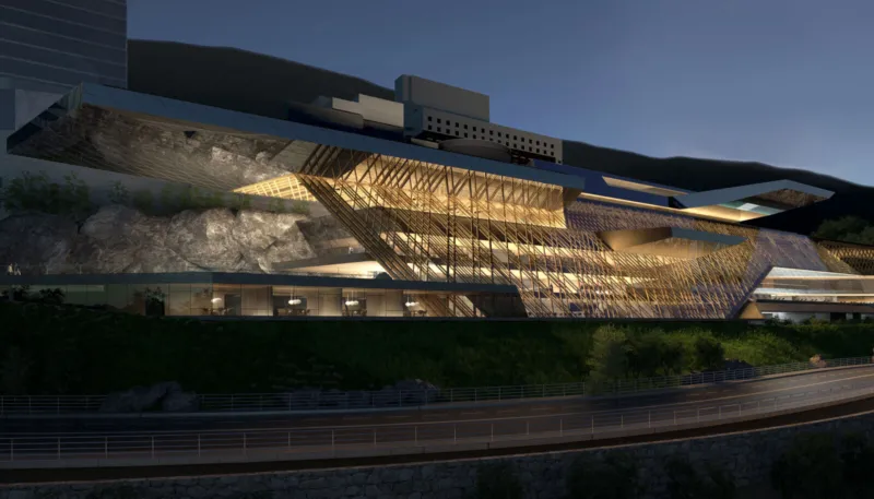 Night view of a contemporary glass-and-wood building with a lattice facade built into a rocky hillside, warmly lit interiors; a curved road in the foreground.