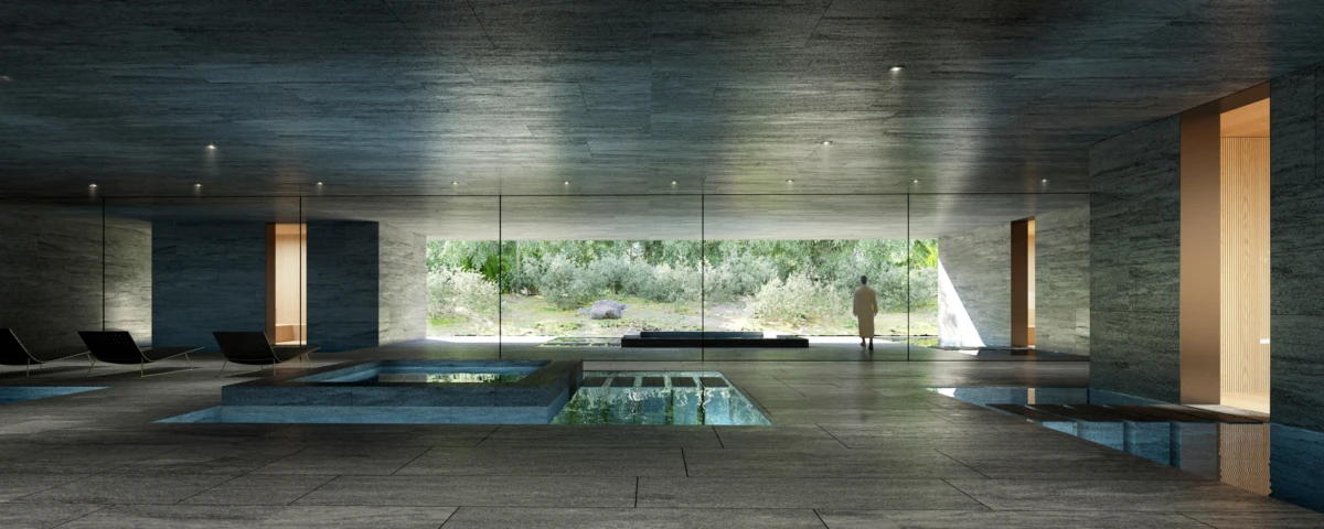 Person standing by a glass wall overlooking a lush garden in a modern indoor spa with pools and lounge chairs.