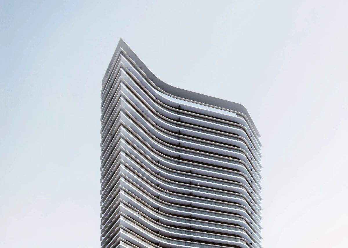 Modern high-rise with stacked curved balconies and a rounded top, set against a pale blue sky.
