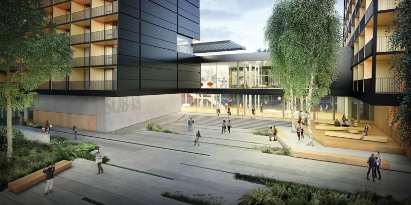 Modern urban plaza with a glass-front building, concrete steps, tiered wooden seating, and people walking or sitting among trees.