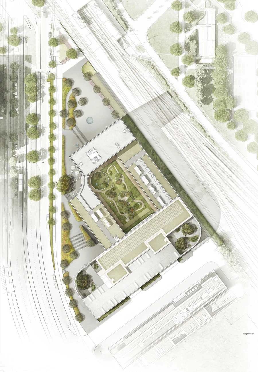 Top-down aerial view of a modern building complex with a central garden courtyard, bordered by trees and parallel railway tracks.