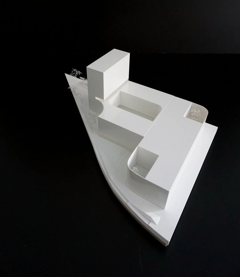 White architectural scale model on a curved base with stacked rectangular blocks forming a hollow central courtyard.