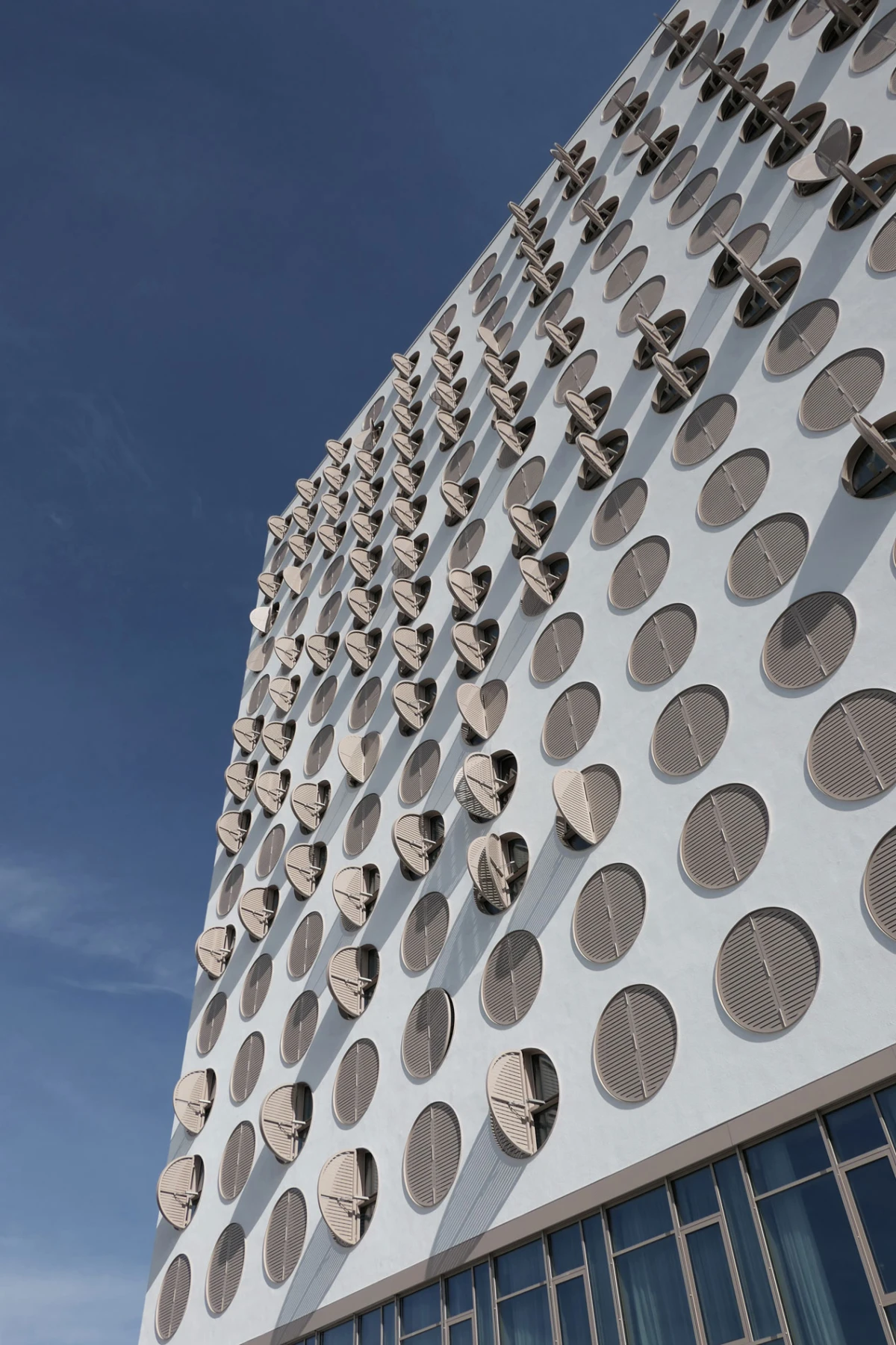 Tilted view of a tall building facade dotted with circular windows against a blue sky.