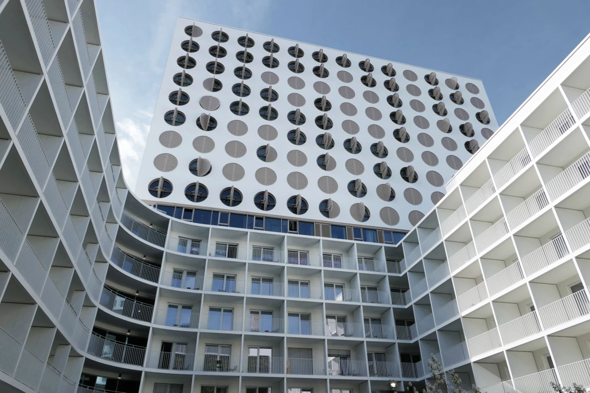 Curved white apartment complex surrounding a central courtyard; upper facade features a grid of circular windows.
