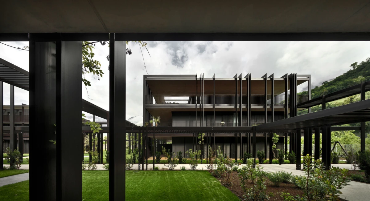 Three-story modern building with open-air walkways supported by black steel columns around a landscaped courtyard.