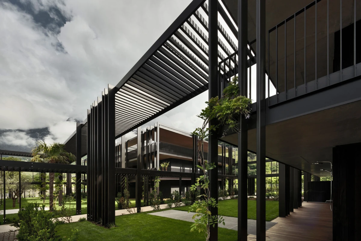 Modern architectural courtyard featuring black steel framework and elevated walkways, with green lawn and small trees.