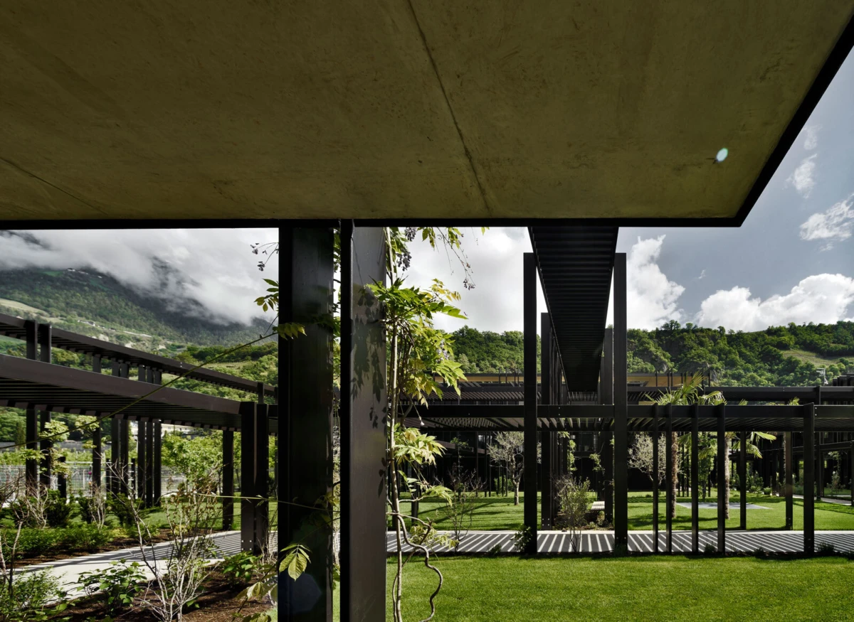 Modern steel-framed walkway over a manicured lawn, with green hills and cloudy mountains in the background.