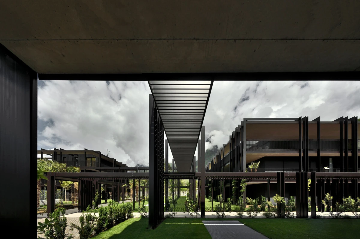 Modern architectural courtyard with steel-framed pergolas and a long central walkway between dark buildings