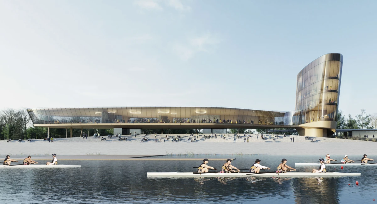 Modern glass riverside complex with a curved cylindrical tower; rowers glide in long boats on the river in the foreground.