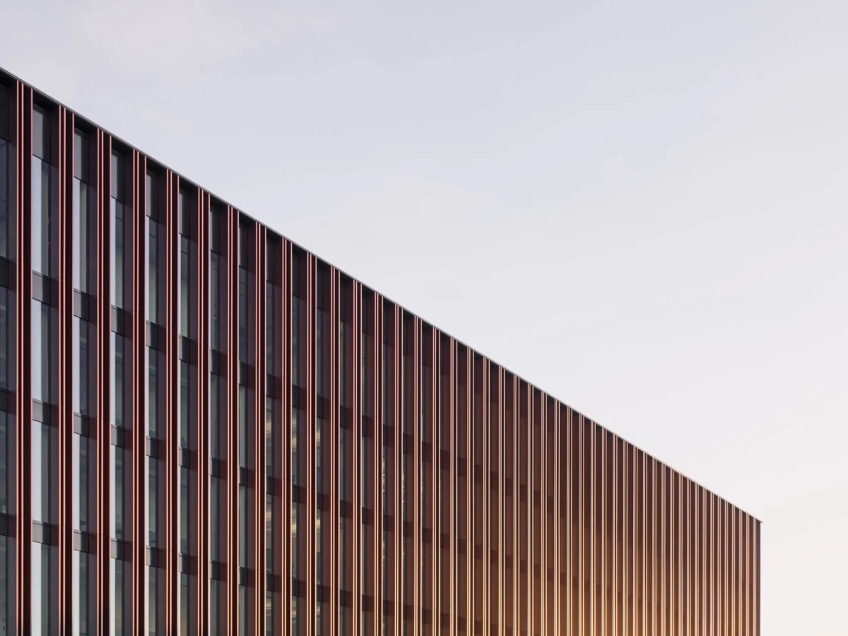 Modern office building facade with orange vertical fins and glass windows, set against a pale sky.