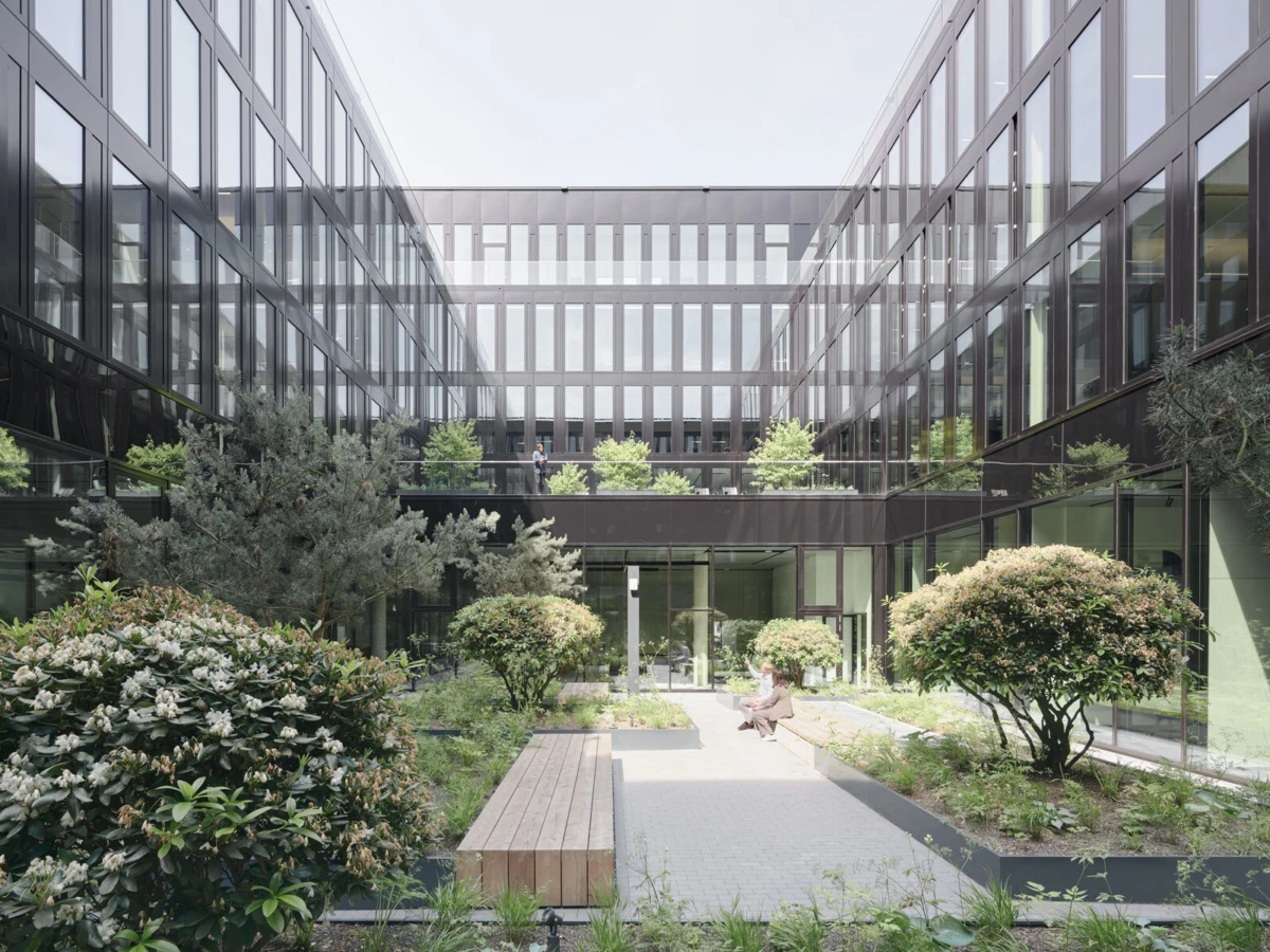 Person sits on a bench in a courtyard garden surrounded by glass office buildings.