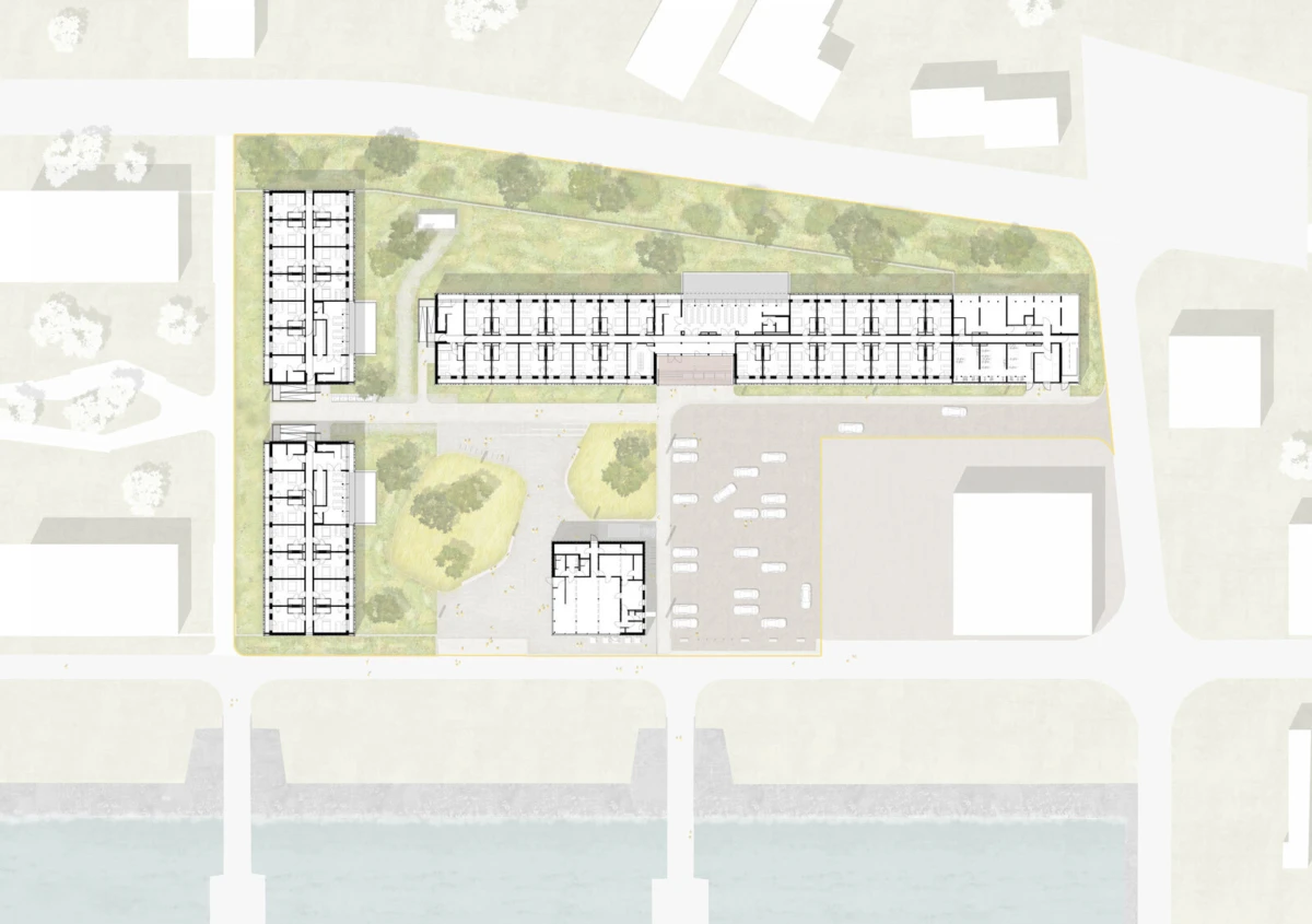 Site plan of a rectangular campus with a long central building and two perpendicular wings, surrounding parking, greenery, and a riverside edge.