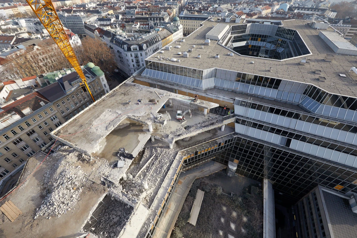 Aerial view of rooftop demolition on a modern glass-office building; rubble, exposed concrete, and a yellow crane against the city.