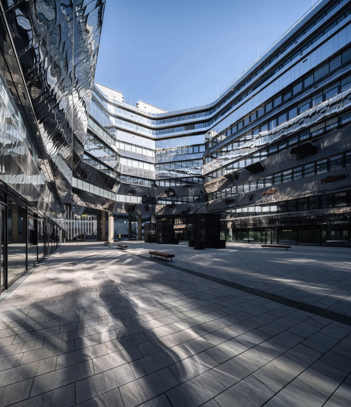 U-shaped plaza between curved, reflective glass office buildings; empty paved courtyard with benches.