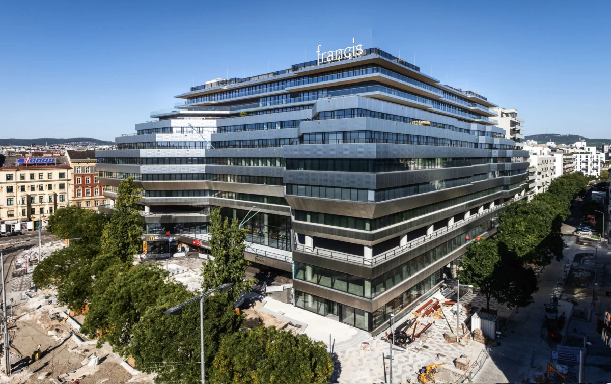 Multi-tiered glass-and-concrete office building with a prominent 'francis' sign atop, in an urban streetscape with trees and construction nearby.