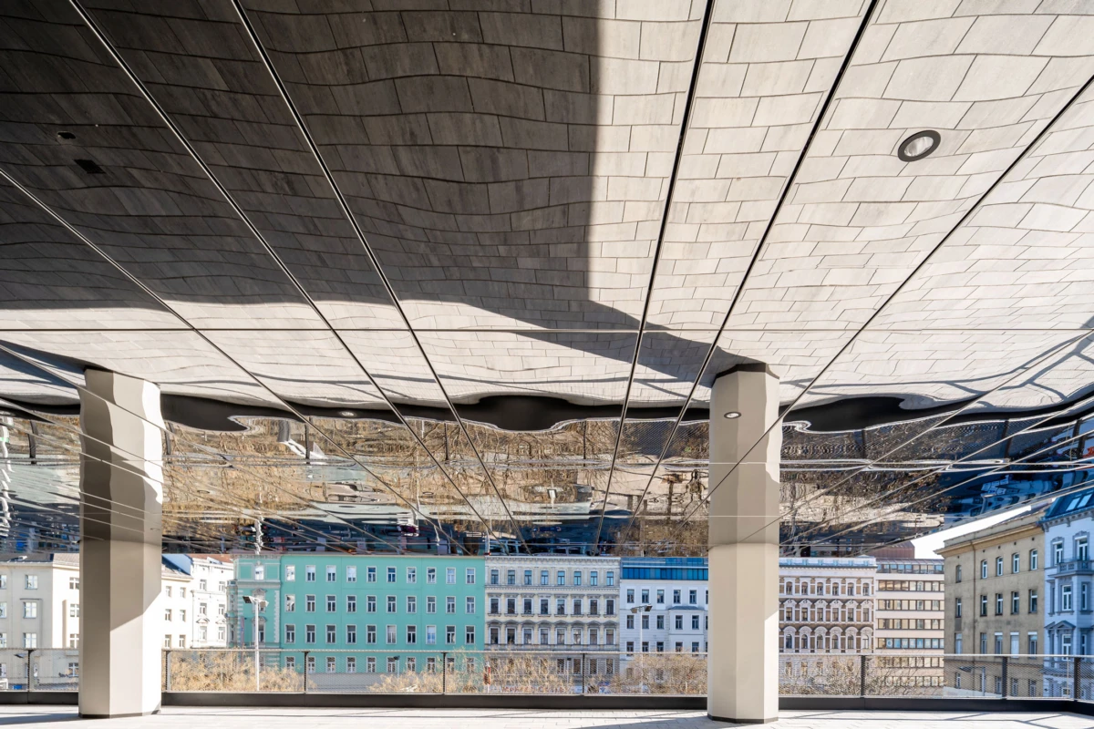 Curved, reflective ceiling above an open terrace with white columns, reflecting an inverted cityscape of pastel buildings.