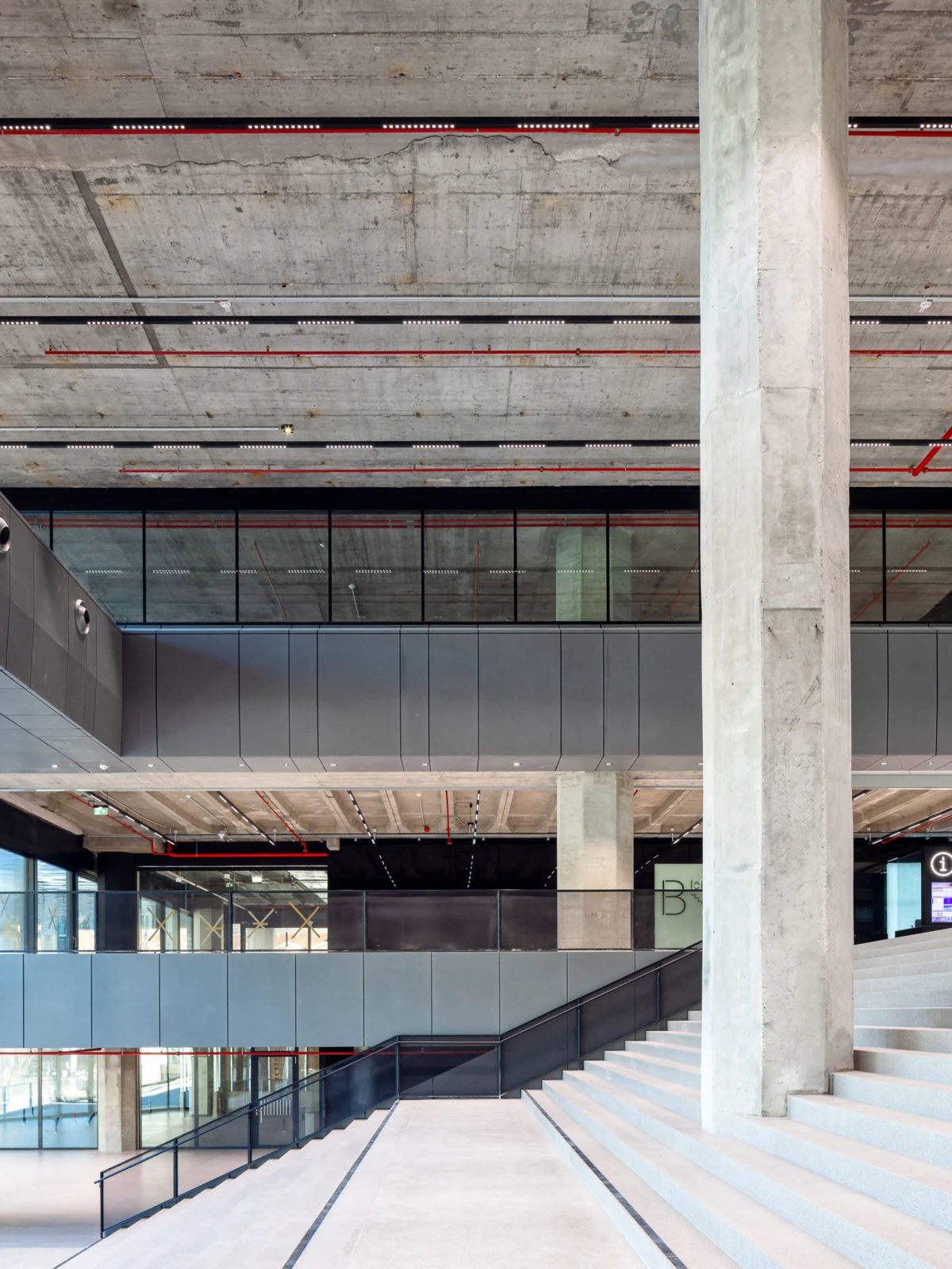 Modern concrete atrium with a tall column, multi-level glass railings, and a broad staircase.