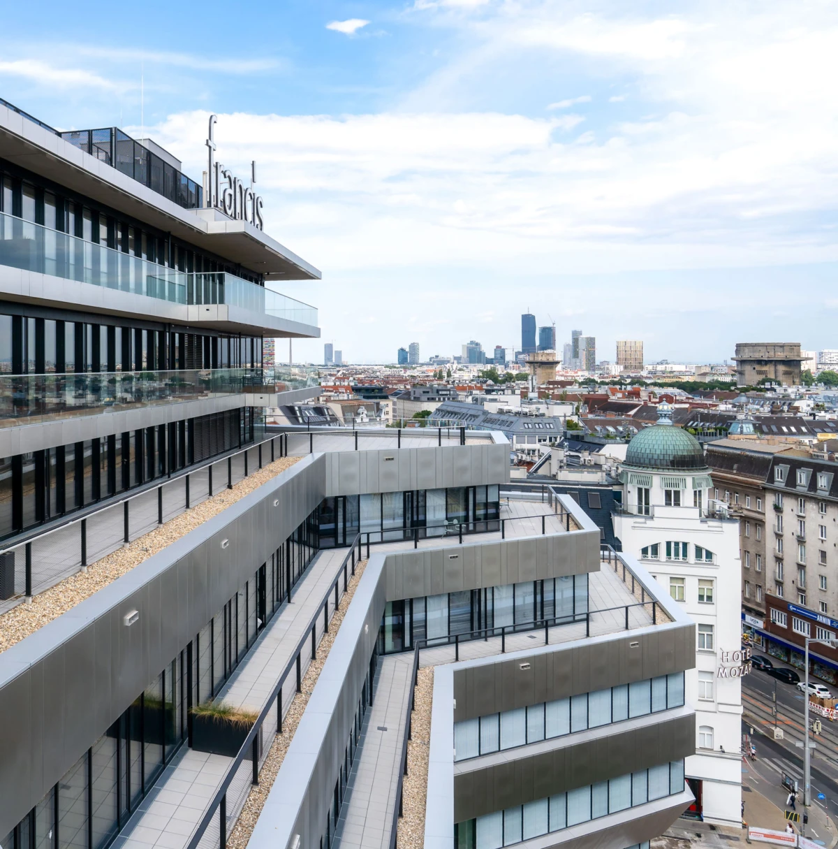 Contemporary multi-story residence with staggered glass balconies and rooftop terraces, overlooking a city skyline with a green-domed building.