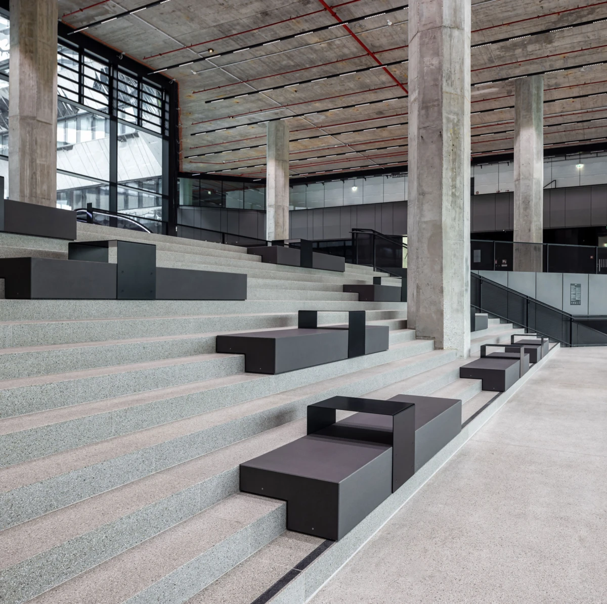 Interior of a modern atrium with concrete stairs and black modular seating blocks on the steps.