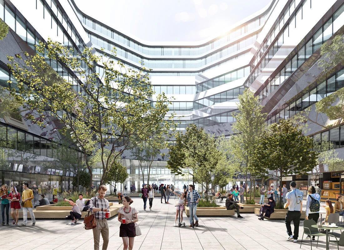 People walk and chat in a modern glass-fronted office courtyard with trees and benches.