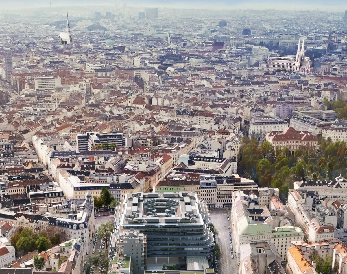 An aerial view of a dense European city with red-tiled rooftops; foreground shows a modern glass office complex, spires in the distance.