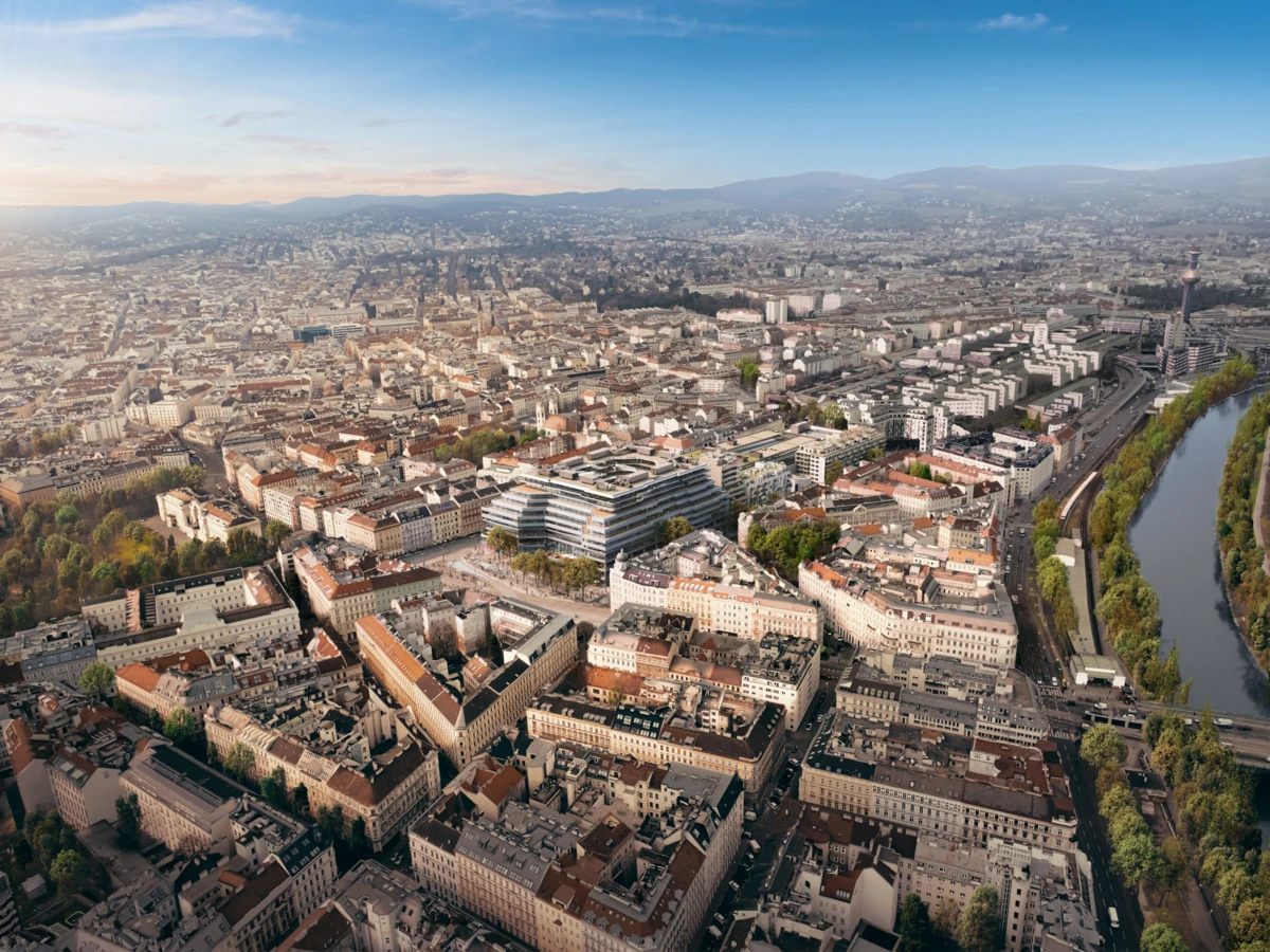 Aerial view of a dense cityscape with a river to the right and distant hills.