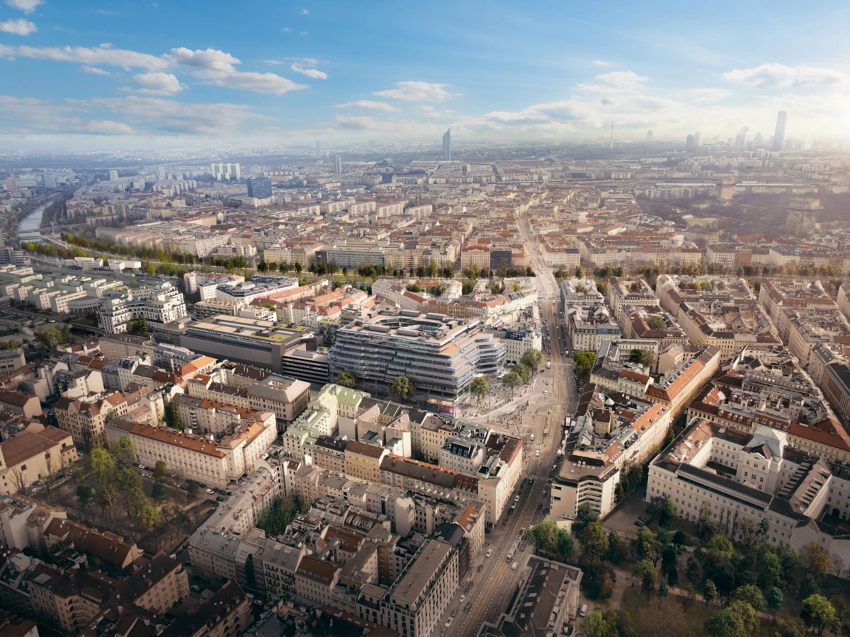 Aerial view of a dense cityscape with grid streets, varied rooftops, and a river on the left under a blue sky.