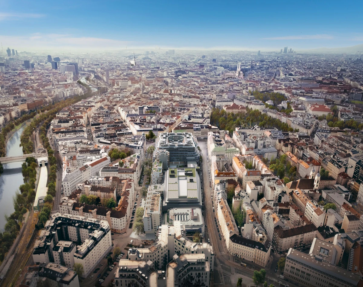 Aerial view of a dense European city with a winding river on the left, bridges, and a central modern complex among historic buildings.